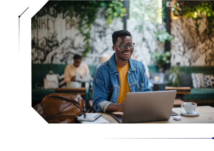 Man in his 20s smiling while using his laptop in a coffee shop