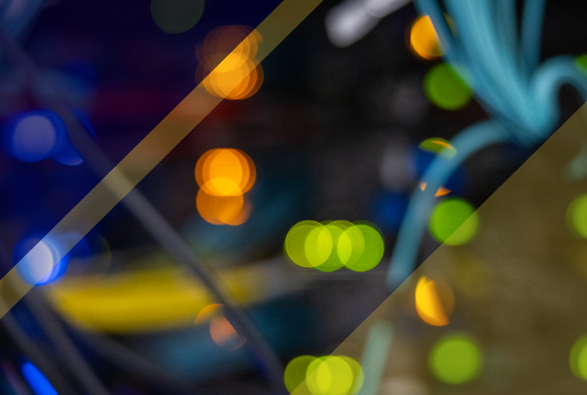 Blurred view of a server rack with cables and glowing indicator lights in blue, green, and yellow, creating an abstract, bokeh-style technical background