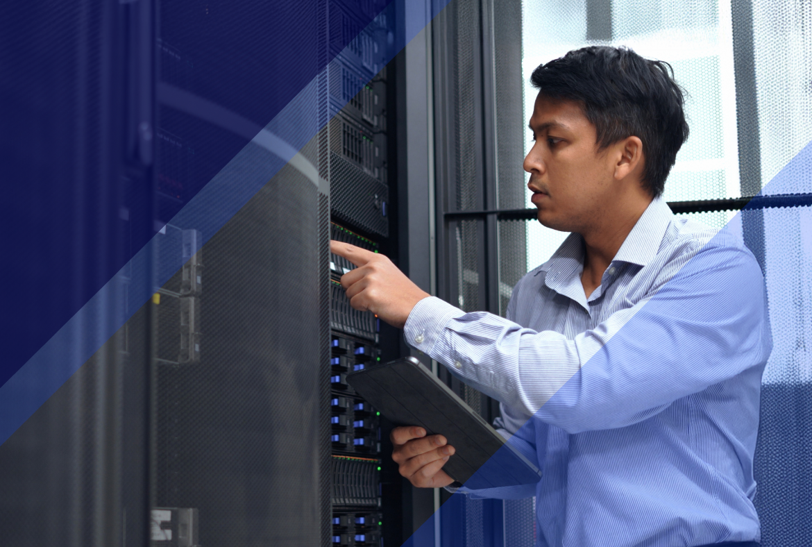 Person holding a tablet and pointing at server equipment inside a data center aisle, inspecting hardware during remote hands support