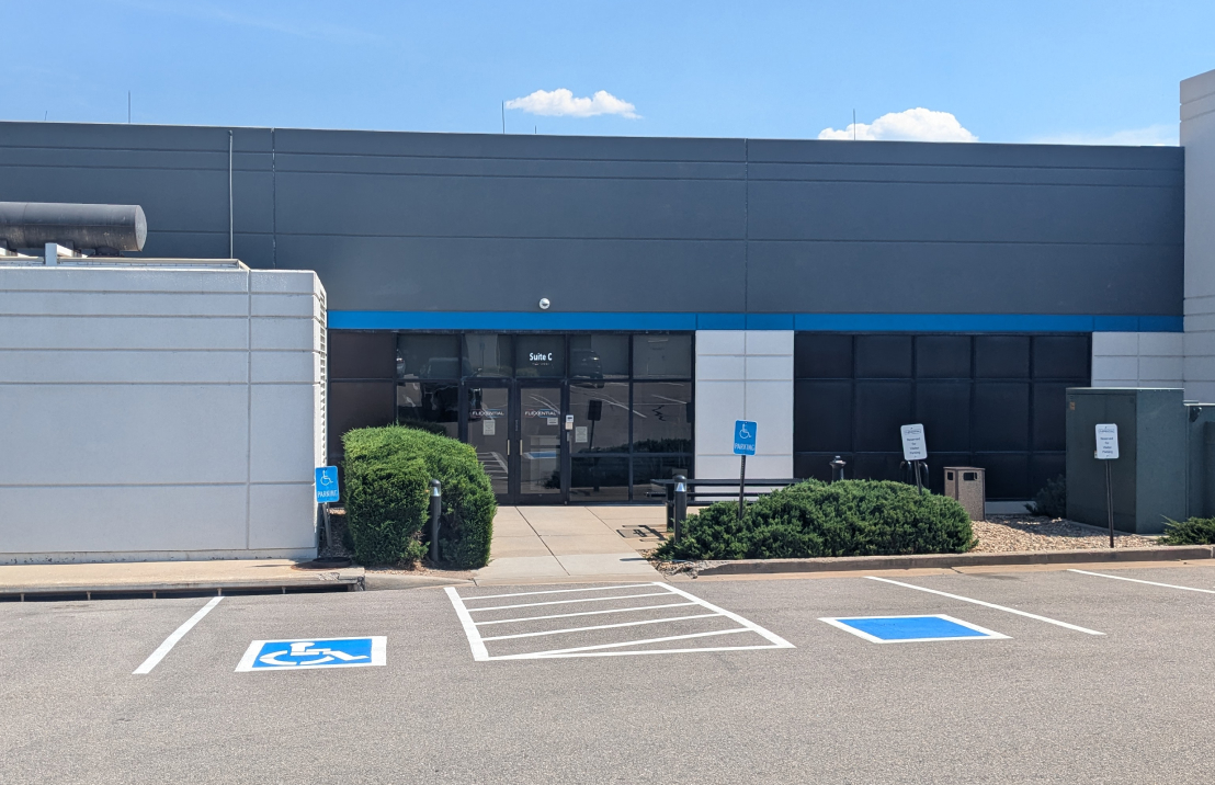 Flexential's Denver - Centennial building with a gray facade, blue accent stripe, glass entrance, and accessible parking spaces in front