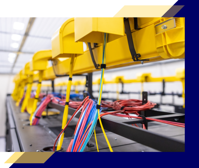 Overhead yellow cable trays in a data center route bundled red, blue, and yellow network cables neatly into black server racks below.