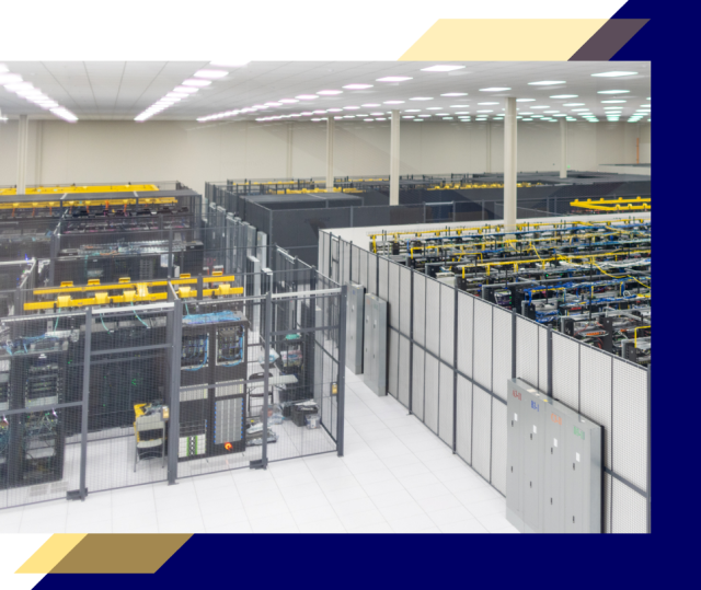 Wide view of a large data center with rows of server cages, yellow overhead cable trays, white floors, and bright ceiling lights throughout the room.