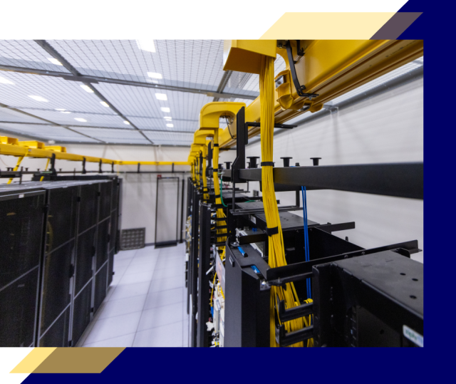 Wide view of a data center aisle with server racks and organized yellow fiber cables routed overhead along cable trays in a clean, brightly lit room.
