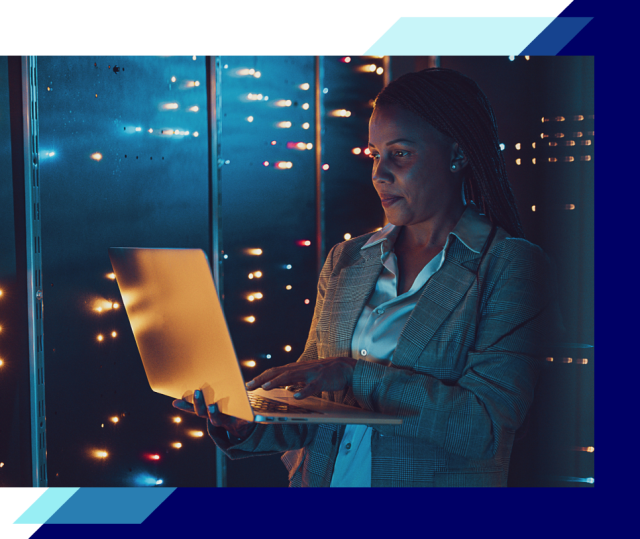 Person using a laptop in a data center aisle, surrounded by server racks with glowing lights, representing managed public cloud operations