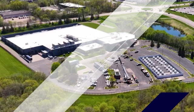 Aerial view of a large data center campus with white-roof buildings, cooling units, parking areas, and surrounding green landscape near roadways