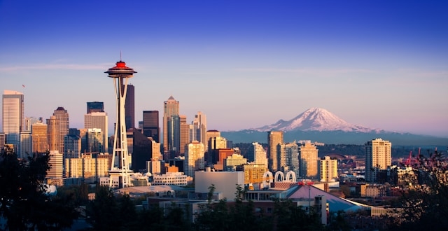 Seattle skyline at sunset with Space Needle, downtown skyscrapers, and Mount Rainier in the distance under a clear blue sky.