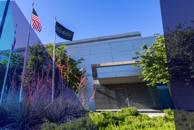 Modern office building with Flexential flag and U.S. flag in front, surrounded by greenery and landscaping under a clear blue sky with blue overlay graphics