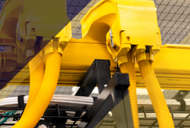 Close-up of yellow cable conduits and connectors on overhead rack in a data center, with bundled cables below and mesh ceiling in background