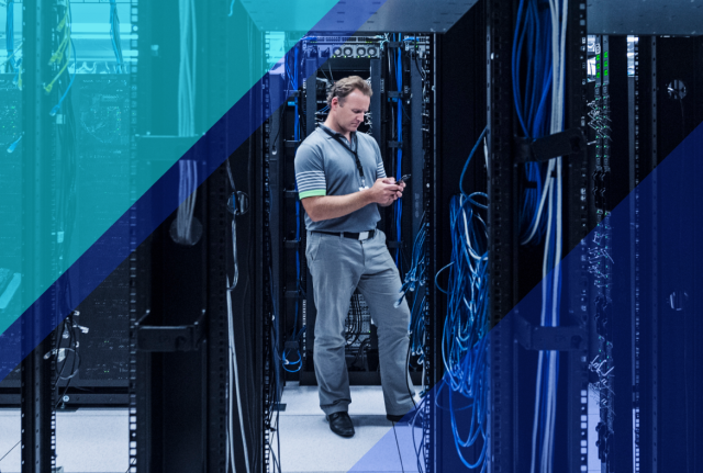 Technician using a smartphone while standing between server racks and network cabling in a data center, with blue geometric overlays