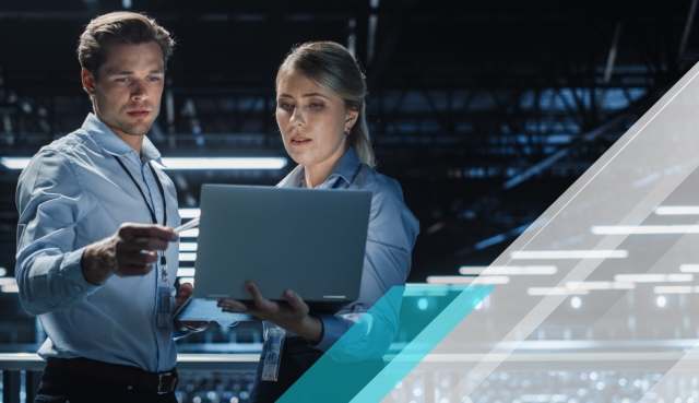 Two professionals reviewing a laptop in a data center, with turquoise and white geometric overlays on the right side.