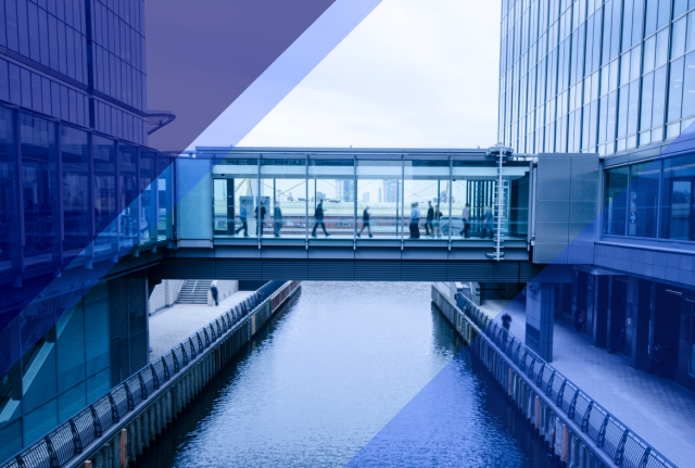 People walking through a glass skybridge between modern office buildings above a canal, with blue geometric overlays
