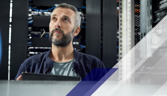 Person using a tablet in a server room, looking upward among data center racks, with blue and gray geometric graphic overlays