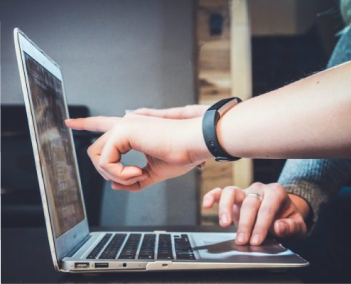 Person pointing at content on a laptop screen while another person uses the keyboard.