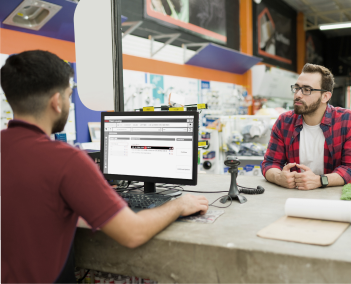 Customer sits across a service counter while an employee uses a computer workstation in a retail store